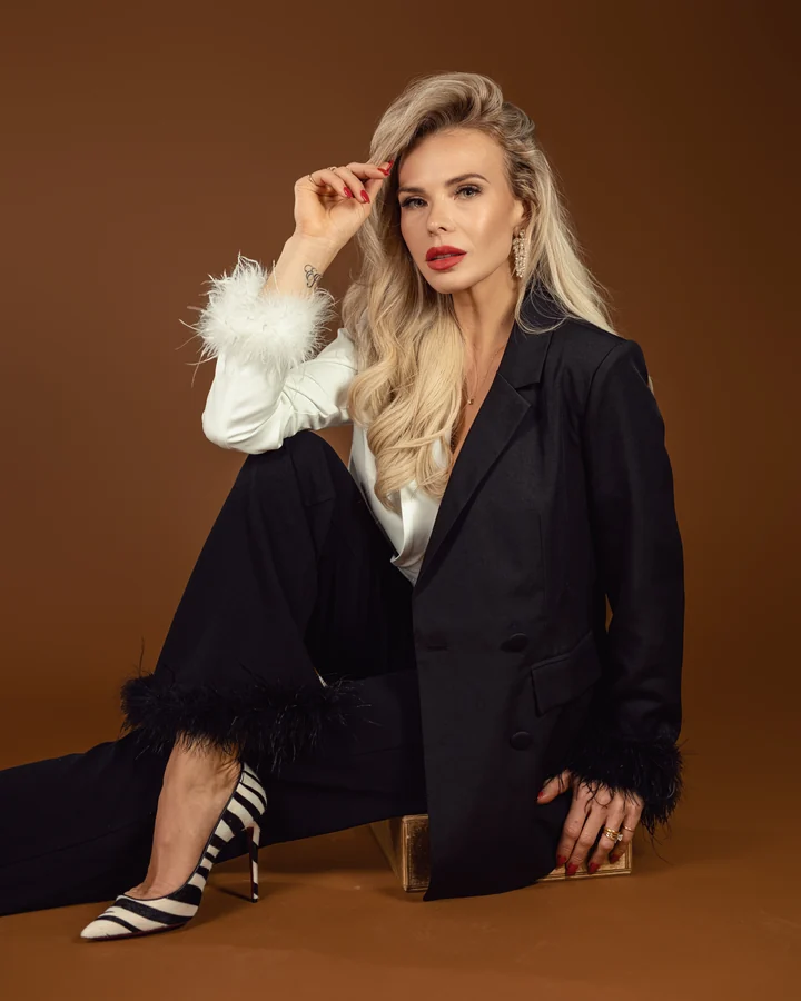 Personal branding portrait of a blonde woman in a black suit with feather cuffs