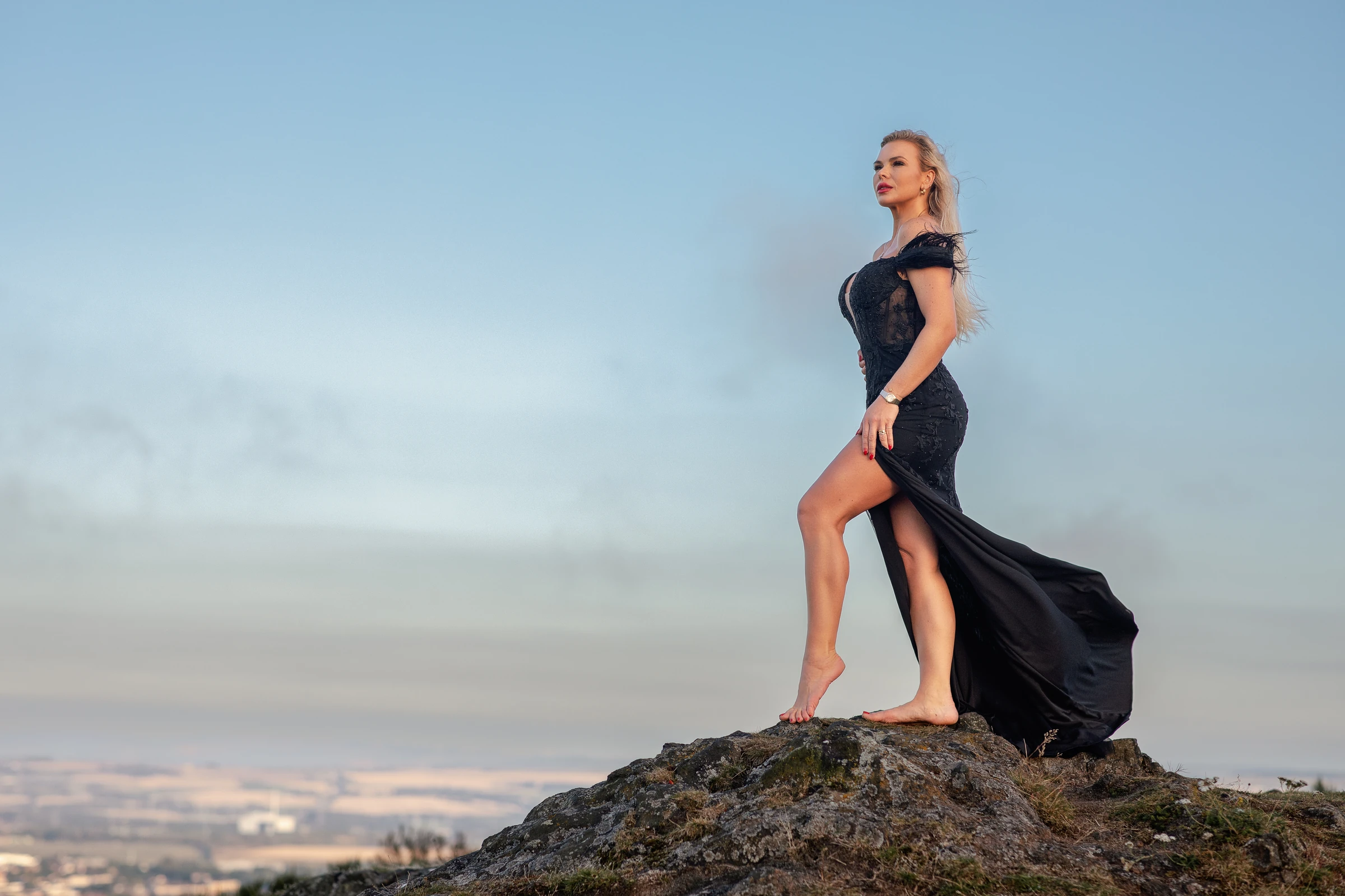 Editorial portrait of a woman in a black gown on a hilltop against a wide sky