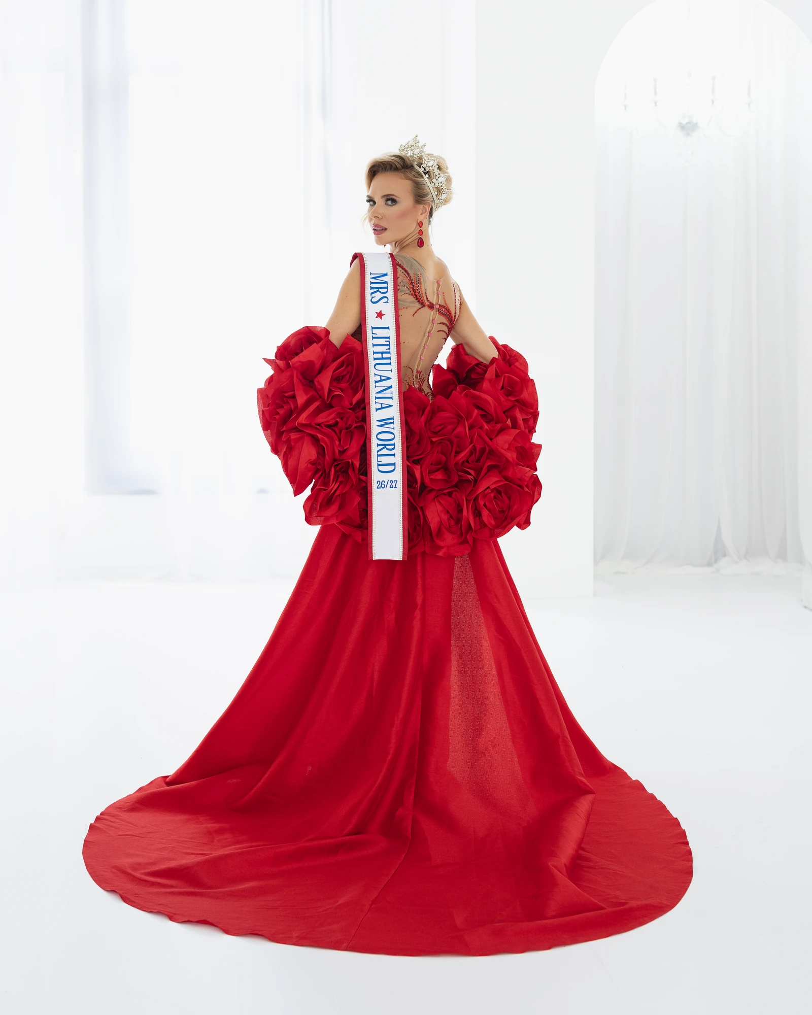 Pageant portrait of a queen in a red ruffled gown wearing the Mrs Lithuania World sash
